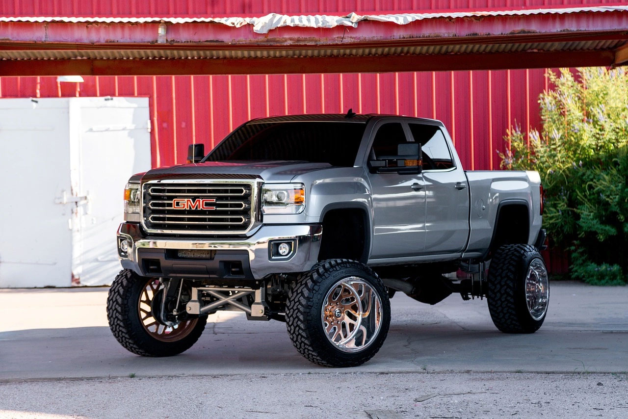 Silver lifted GMC 4x4 truck with large off-road tires parked in front of a red building.
